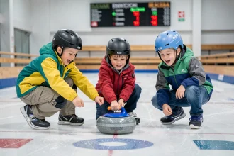 Jeunes enfants en train de pousser une pierre de curling adaptée sur une patinoire intérieure lors d'une initiation sportive